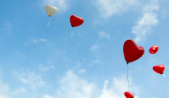 unos globos en forma de corazon vuelan por el cielo